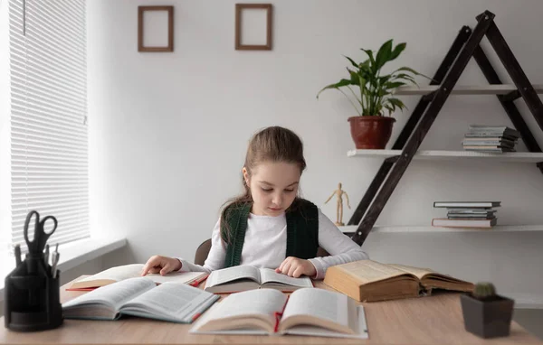 Συγκεντρωμένη Καυκάσια μαθήτρια κάθεται στο γραφείο της με ανοιχτά βιβλία και εγχειρίδια να κάνει τα μαθήματά της ενώ σπούδαζε στο διαδίκτυο. Το παιδί είναι μόνο στο σπίτι.. — Φωτογραφία Αρχείου