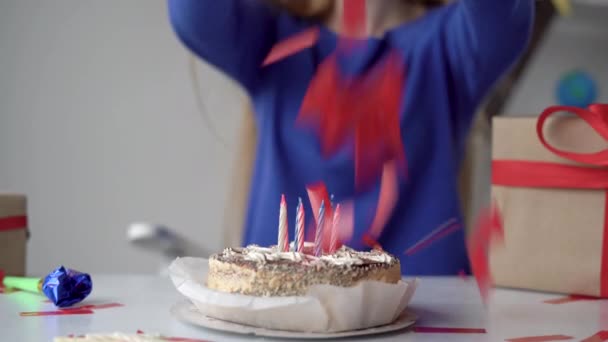 Primer plano de un pastel de cumpleaños con velas sin encender está sobre la mesa. La mujer le lanza confeti. El concepto de fuegos artificiales en casa en honor al cumpleaños. — Vídeos de Stock