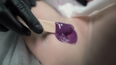 Usta bir kozmetikçi, karıştırıcı macun kullanan genç bir kadının koltuk altlarındaki kılları almak için bir prosedür uygular. Güzellik ve vücut bakımı kavramı. Yakın plan..