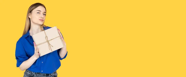 Krásná žena stojící na žlutém pozadí oblečená v modré košili a držící v rukou krabici s řemesly. Baner — Stock fotografie