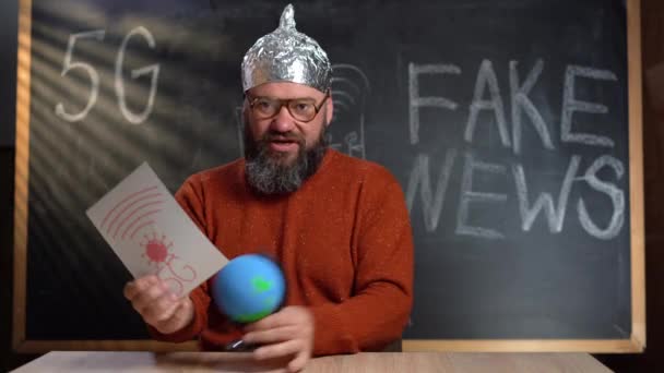 A strange man in a foil hat with a Stop 5G poster. Conspirational fake news. takes off his hat and puts it on the globe. The concept of protection from special services. 4k — Stock Video