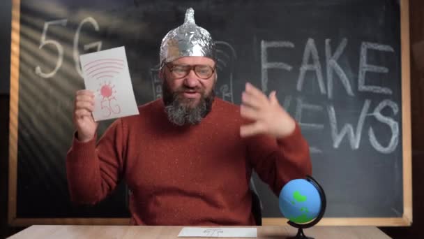 Ένας γενειοφόρος, αστείος Καυκάσιος με καπέλο από αλουμινόχαρτο, μεταδίδει στο σπίτι του στο στούντιο. Μιλάμε για θεωρίες συνωμοσίας. Βλάβη των τεχνολογιών 5g. Κατάληψη του κόσμου. — Αρχείο Βίντεο