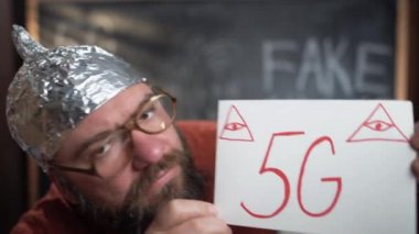 Caucasian bearded man with glasses and a foil cap. Holds a tablet with the text 5g. Pulls out a burner and ignites. Conspiracy theory. A call to destroy the towers.