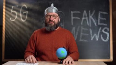 Folyo şapkalı beyaz sakallı genç bir adam tebeşir tahtasında oturuyor. Değişikliğe ihtiyacımız olduğunu söyleyen bir işaret kaldırıyor..