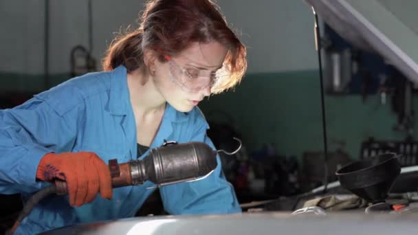 Mujer caucásica mecánico de automóviles haciendo una inspección de coches en su taller. Él sostiene una lámpara en sus manos y busca una avería cuidadosamente. — Vídeo de stock