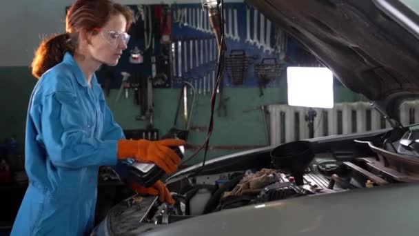 Mulher mecânico de automóveis perto do capô aberto do carro. substituição e enchimento de óleo no motor de uma estação de serviço. — Vídeo de Stock