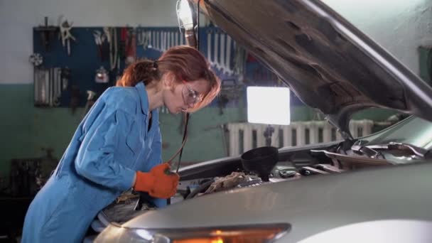 Μια όμορφη γυναίκα μηχανικός ενδυνάμωση εργάζονται σε ένα αυτοκίνητο σε μια υπηρεσία αυτοκινήτων. Μια γυναίκα με γυαλιά επισκευάζει μια μηχανή. Χρησιμοποιεί καστάνια. πραγματικό αυθεντικό εργαστήριο. — Αρχείο Βίντεο