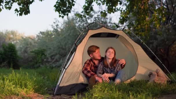 Vrolijk meisje en een jongen brengen tijd samen door op de camping. Gelukkige vrouwelijke en mannelijke toeristen zitten bij zonsondergang in een palet en knuffel. — Stockvideo