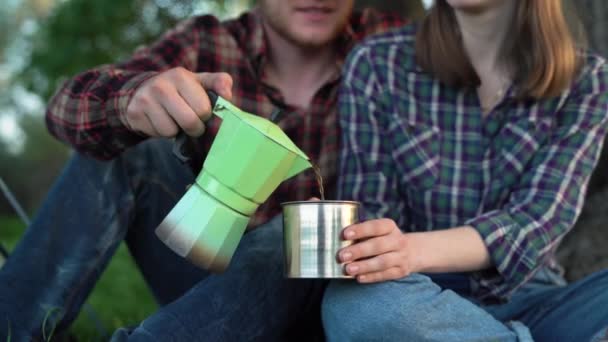 Man resenären häller färskt varmt kaffe till kvinnan från gejser kaffebryggare i metall kopp bland landsbygden örter. Lugnande ögonblick. Alternativ kaffekokning under resan. — Stockvideo