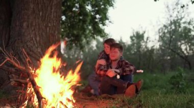 Yazın ateşin yanında oturan beyaz erkek ve kadın ellerinde lokumlarla çubuk tutuyorlar. Huzur içinde yat. Mutlu, sevgi dolu bir çift akşam kampta sarılıyor..