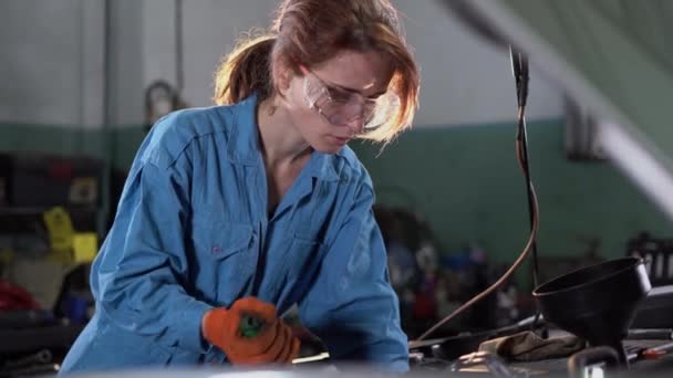 Ritratto di una donna meccanico che lavora in un servizio di auto. Potenziare una donna che ripara un motore. Aprire il bagagliaio, riparare il motore. Gira il cricchetto. Un vero e proprio laboratorio atmosferico. — Video Stock