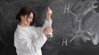 Okulda bir kadın öğretmen ya da kimya öğretmeni, kimyasal formüllü bir tahtanın arka planında duruyor. Beyaz tıbbi önlük ve gözlükler. Elinde bir matara tutuyor ve bir deney yapıyor. konsept okula geri döndü.