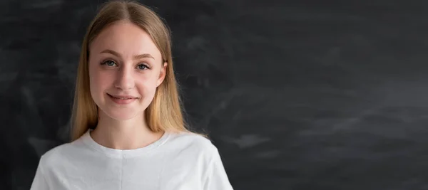 Primer plano de una estudiante caucásica con el pelo largo cerca de la pizarra de tiza se encuentra en el aula. Profesora universitaria y de aula. Lugar para texto y banner. Concepto educativo. — Foto de Stock