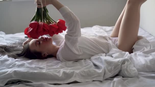 Boldog nő fekszik az ágyon a szobában. Egy gyönyörű csokor vörös tulipán egy lány kezében. Szép virágillat..