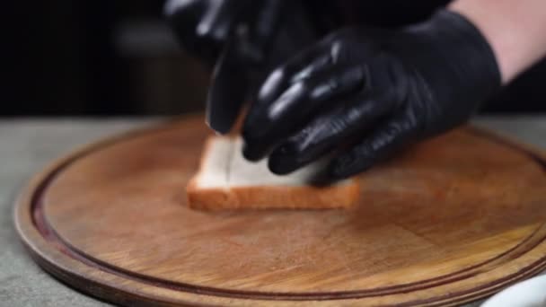 Primer plano de una mano de chefs con guantes negros. Corta el pan en trozos pequeños con un cuchillo grande. Preparar ensaladas rusks. — Vídeos de Stock