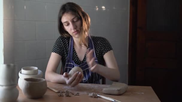Een vrouwelijke pottenbakker zit thuis aan een tafel en kneed een stuk klei in haar handen. Kleine bedrijven en productie van handgemaakte souvenirs. — Stockvideo
