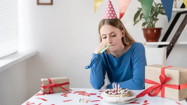Вечірка не є успішною сумною кавказькою жінкою нудно сидіти наодинці за столом з тортом і подарунками. Щаслива дівчина святкує свій день народження сама. Концепція домашнього свята . — стокове фото