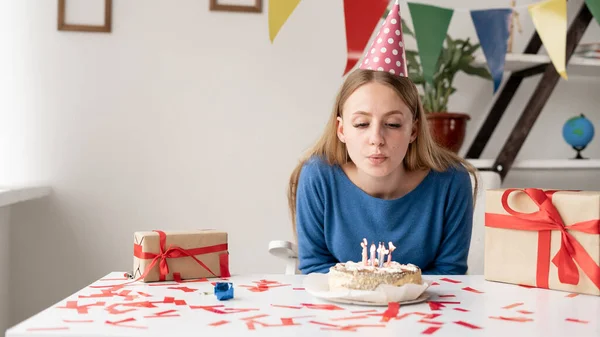 Кавказская деловая леди и молодая девушка задувают свечи на торте в свой день рождения, празднуя дома или в офисе. Один человек в праздничной шляпе на рабочем месте. — стоковое фото