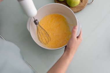 Dalış blenderi ve çırpma kabıyla, kız yumurtaları seramik kızartma tavasında çırpıyor. Ev yapımı için para kazanma süreci. Turta pişiriyorum..