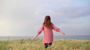 Free carefree girl enjoying summer nature and sun in the park on the lawn. Happy childhood and family concept. The child plays in the street, runs away across the field, arms out to the sides.