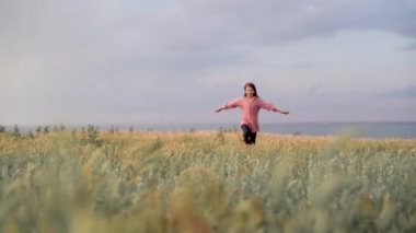 A young Caucasian girl runs in the summer in the park at sunset on a green meadow. A fun and carefree childhood.