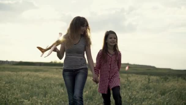 Mother and daughter of a child walking in the meadow in the evening at sunset. mom and little girl, child are walking along an agricultural road in a field of flowers. Fun family time. — 图库视频影像