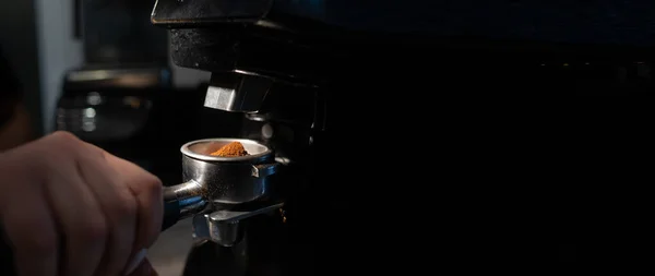 Nahaufnahme eines Baristas, der in einem Café einen Portafilter mit Kaffee vor einer elektrischen Kaffeemühle hält. Das Konzept der Zubereitung von Bohnen für den morgendlichen Espresso in einem Café — Stockfoto