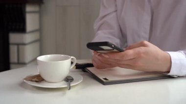 İş kadını bir kafede oturmuş mesaj ya da telefon mesajı yazarken çalışıyor. Elinde akıllı telefon ve masanın üstünde not defteri olan bir elin yakın çekimi. İnternetteki uzaktan çalışma kavramı