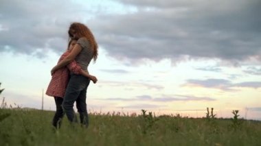 Anne, güzel bir günbatımının arka planında kızına nazikçe sarılıyor. Mutlu aile kavramı. Yetişkin bir kız, annesinin kollarında gün ışığında bir tarlada. Anne kızının saçını okşuyor..