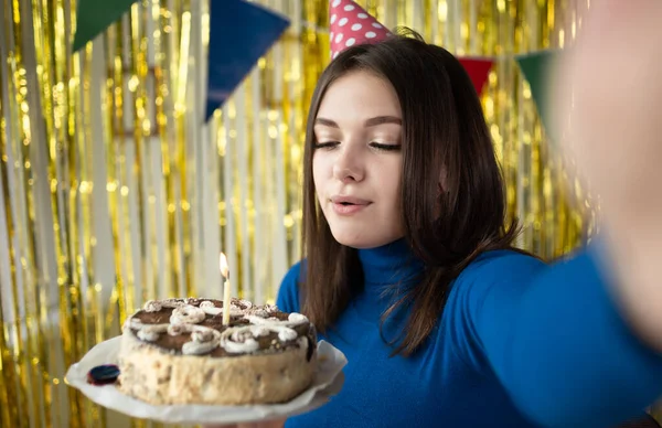 一个黑发女孩的特写在生日蛋糕上吹灭了一支蜡烛，同时在她生日的时候把蜡烛放在相机前。一个人在家吃卡路里自制蛋糕的年轻女人. — 图库照片