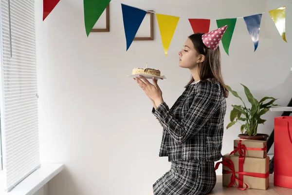 Születésnap az irodában. Egy fiatal kaukázusi hölgy szülinapi tortát tart a kezében és elfújja a tüzet.. — Stock Fotó