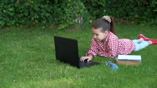 Jong meisje schoolmeisje. Vrouw werkt op laptop computer in het stadspark op groen gras zonlicht buiten gazon. Mobiel kantoor. Bedrijfsconcept voor freelancers. — Stockvideo