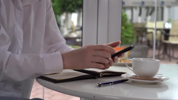 Imagen de cerca de una mano de mujer sosteniendo un teléfono móvil. mujer joven lee las noticias en un teléfono móvil mientras está sentada en un café. — Vídeo de stock