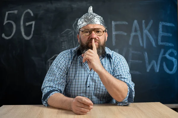 conspiracy theories schizophrenic strange man in glasses and a hat holding a finger near his mouth reveals a conspiracy theory on earth. The abnormal man in the room closes his mouth.