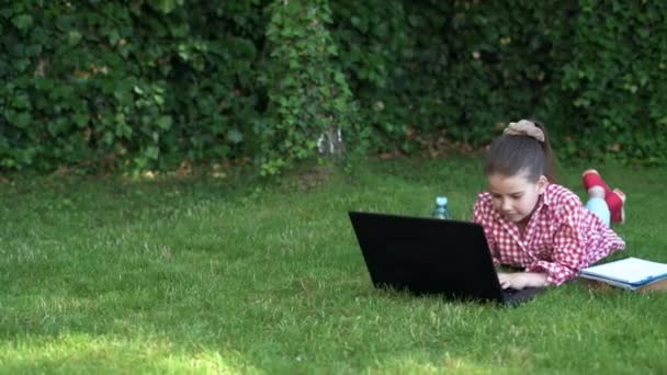 Echt geluk. gelukkig meisje zittend op groen gras met laptop. Wegwezen. Het kind speelt een computerspel. terug naar school. online onderwijs. Dag van kennis. kind leert een privéles. bloggen. — Stockvideo