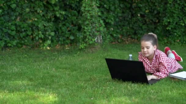 야외 오락 과 블로그. 한 여학생은 노트북 근처 공원의 풀밭에 누워 노트북으로 타자를 치고 있습니다. 과학 기술 과 인터넷. — 비디오