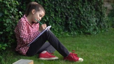 Güzel kız dışarıda dinleniyor. Güneşli bir günde yeşil çimlerde oturan kız öğrenci telefonla iletişim kuruyor ve not defterine not alıyor. Mobil iletişim konsepti.
