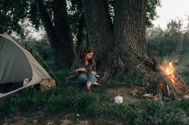 Ormandaki genç bir kadın bir ağacın altında oturur ve marşmelovları ağaçların dallarına gerer. Kamp yapmak ve çadır kurmak. Yazın açık hava yemekleri. Lokum kızartmak için şenlik ateşi ve alev.