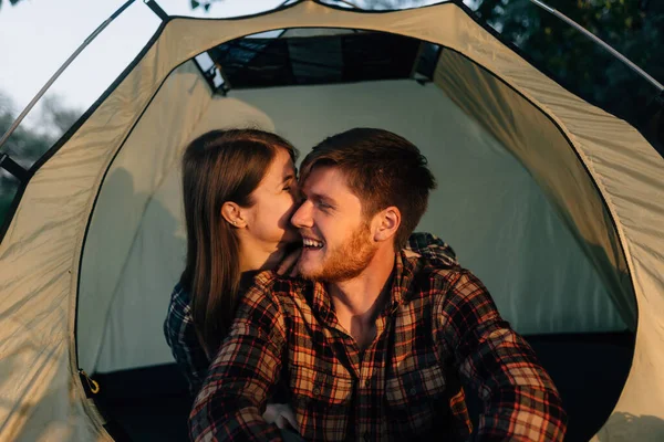 Primer plano de una pareja amorosa en una tienda de campaña, un tipo barbudo y una chica caucásica en camisas. El resto de una familia joven al aire libre. Tarde y puesta de sol en el bosque. Los viajeros descansan. — Foto de Stock