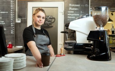Kafkasyalı bir barmen kız bir kafede ya da barda bir müşteriye bir fincan sıcak kahveyi uzatıyor. Dükkanda kahve satıyorum. Kafeterya ve üniformalı satıcı..