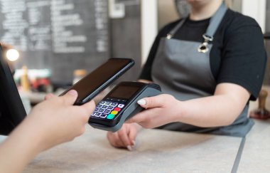 Bir kadın telefonu NFS teknolojisiyle öder telefondaki bir kafede ya da kafeteryada irtibatsız bir terminalle. NFS teknolojisi ile sipariş ödemesi için cep telefonu.