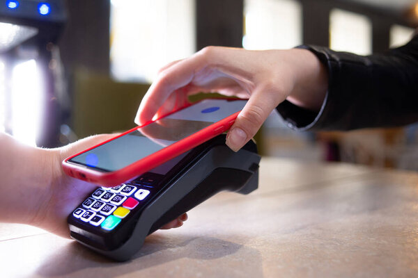Close-up of a customer using their cell phone or smartphone and NFS technology to pay a barista for a purchase in a cafe or store. The concept of payment by card.