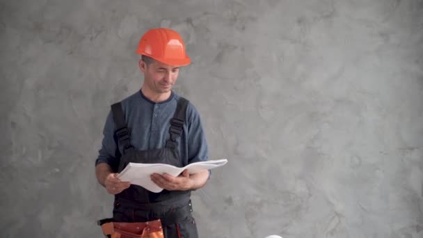 Um trabalhador da construção tem uma folha de papel nas mãos. Um homem na forma de um construtor. — Vídeo de Stock