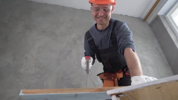 Alt manzara, üniforma giyen ve kafasında turuncu bir şapka olan bir inşaat işçisi tahta bir tahtayı testereyle kesiyor. Boşluğu kopyala. — Stok video