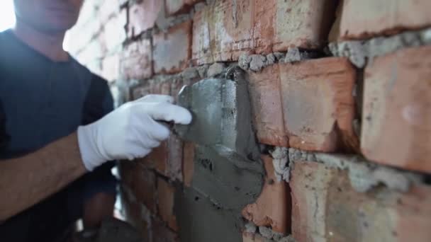 Close-up van de handen van een mannelijke bouwer, hij pleistert een bakstenen muur met behulp van gips. woningrenovatieconcept. — Stockvideo