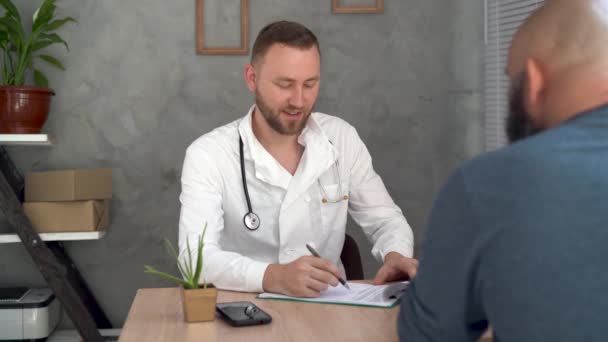 A man at the doctors appointment sits at the table and talks about his health. Doctor examination concept. — Stock Video