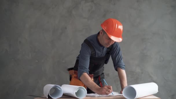 Arquiteto masculino ou engenheiro trabalhando em casa desenhando um projeto de construção. Vestido com um uniforme e um capacete laranja. — Vídeo de Stock