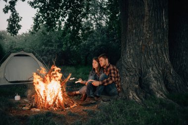 Aşıklar ateşin başında oturur ve şekerleme kızartırlar. Ormanda kamp yapmak. Sevgili erkek ve kız gezginler yemek hazırlıyorlar. Açık hava turizmi ve eğlence konsepti. Metin için yer