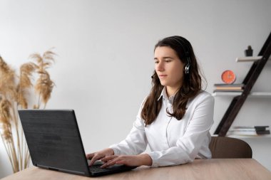 Bilgisayarlı kablosuz bir kulaklıkla evde çalışan odaklanmış bir öğrenci. Kulaklıklı kız operatör klavyede yazı yazıyor. İnternet bağımlılığı ve online oyunlar. yan görünüm