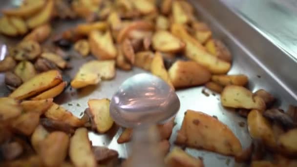 Närbild av en metallsked på en matservering linje i en buffé plockar upp en rustik maträtt av stekt potatis med kantareller eller champignons låg på en vit platta. — Stockvideo